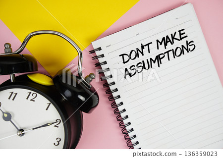 Don't Make Assumptions text written on notepad with alarm clock on pink background 136359023