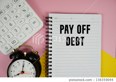 Pay Off Debt text written on notepad with calculator and alarm clock on pink background Pay Off Debt text written on notepad with calculator and alarm clock on pink background 136359044