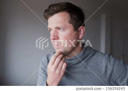 Pensive young man standing at home thinking about problems and making decisions Pensive young man standing at home thinking about problems and making decisions 136359245