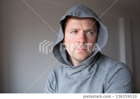 Lonely depressed man wearing a hoodie standing alone and hiding his face from the public 136359310