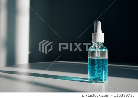 Dropper bottle containing blue liquid two-phase skincare serum on table with harsh shadow Dropper bottle containing blue liquid two-phase skincare serum on table with harsh shadow 136359755