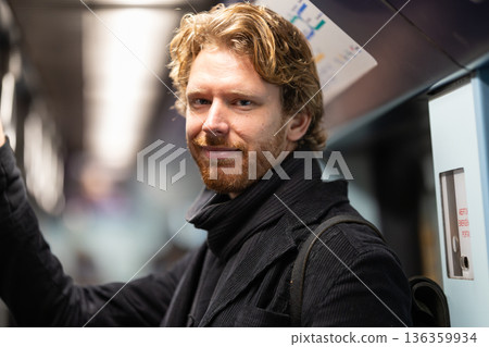 Young man riding subway train smiling, commuting daily Young man riding subway train smiling, commuting daily 136359934