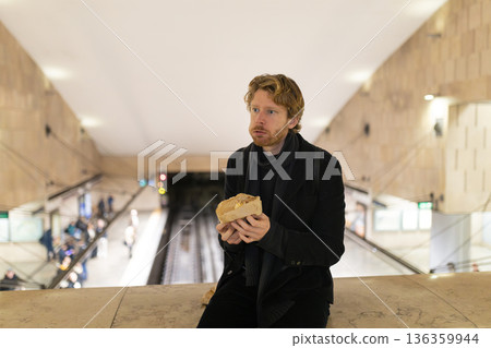 Man eating sandwich in subway station platform 136359944