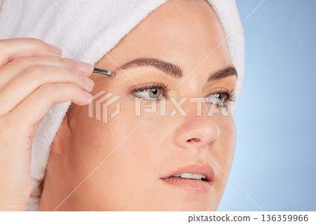 Face, beauty and woman with tweezers for eyebrow in studio, blue background and aesthetic change. Closeup of female model, epilation tools and hair removal for grooming brows, facial skincare or glow 136359966