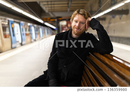 Young man smiling sitting at subway station platform Young man smiling sitting at subway station platform 136359980