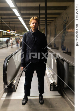 Man standing on moving walkway in urban transport station 136359982
