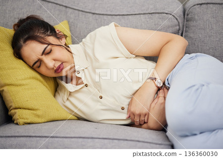Sick woman, stomach and pain in home for gastric health, digestion and colon emergency. Female person with stress, menstruation and abdomen risk of constipation, anxiety and endometriosis on sofa 136360030