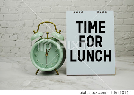 Time For Lunch with green vintage alarm clock against a white brick wall background. Time For Lunch with green vintage alarm clock against a white brick wall background. 136360141