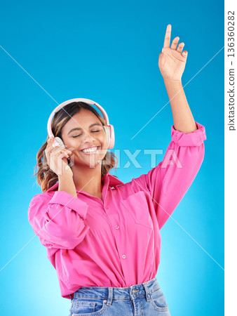 Happy woman, headphones and listening to music, audio streaming service and techno or student podcast in studio. Young person dance to radio for wellness and electronics on a blue gradient background Happy woman, headphones and listening to music, audio streaming service and techno or student podcast in studio. Young person dance to radio for wellness and electronics on a blue gradient background 136360282