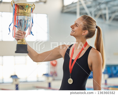 Swimming, trophy and winner in celebration with medal, achievement or happiness from success in the race or pool. Winning, competition and woman swimmer or athlete on sports podium with gold award 136360382
