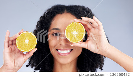 Portrait, skincare and woman with lemon eye for wellness or nutrition in grey studio background. Happy face, girl and vitamin c for dermatology with smile, fruit, diet or natural facial treatment. 136360422