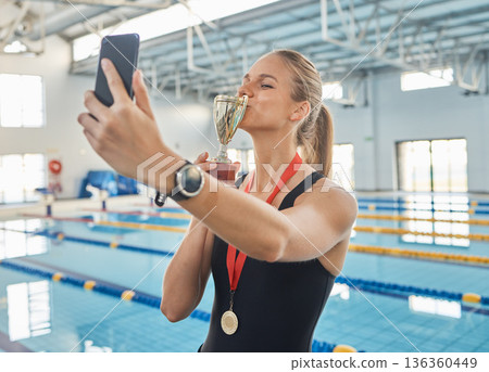 Swimming woman, trophy and selfie by pool, kiss and success in sports, competition and social media post. Girl, athlete or champion with gold medal, memory and profile picture on web blog for goals Swimming woman, trophy and selfie by pool, kiss and success in sports, competition and social media post. Girl, athlete or champion with gold medal, memory and profile picture on web blog for goals 136360449