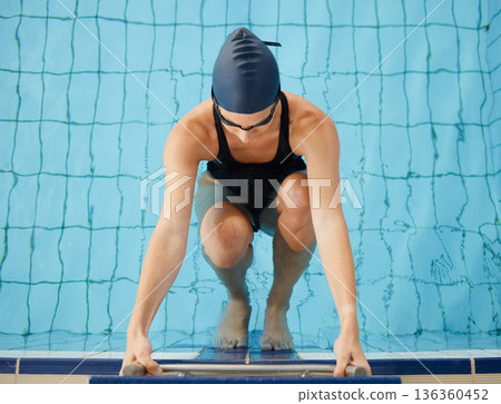 Swimming, start and top view of woman in pool for exercise, training and workout for competition in gym. Fitness, water sports and female swimmer on starting block for race, challenge and performance Swimming, start and top view of woman in pool for exercise, training and workout for competition in gym. Fitness, water sports and female swimmer on starting block for race, challenge and performance 136360452