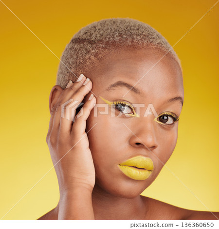 Portrait, cosmetics and african girl with creative for glow in yellow studio with background in closeup. Woman, serious and skincare with bright makeup with hand on face for dermatology or wellness. Portrait, cosmetics and african girl with creative for glow in yellow studio with background in closeup. Woman, serious and skincare with bright makeup with hand on face for dermatology or wellness. 136360650