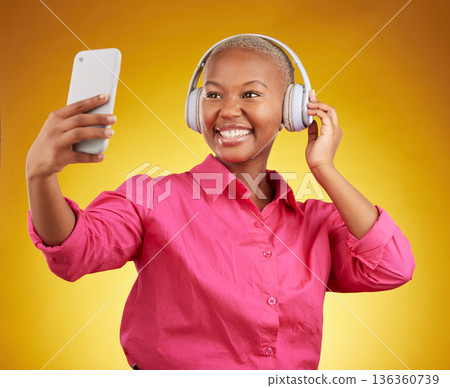 Smile, selfie and black woman with headphones for music, radio and podcast in studio isolated on a yellow background. Profile picture, photographer and African person or influencer on social media 136360739