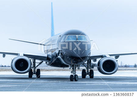 Close-up front view of a black passenger airplane taxiing at winter airport Close-up front view of a black passenger airplane taxiing at winter airport 136360837