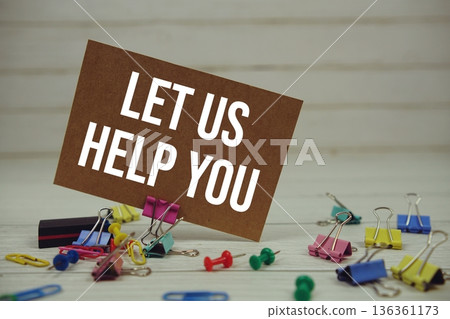 Let Us Help You text on paper card with stationary on wooden background Let Us Help You text on paper card with stationary on wooden background 136361173