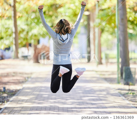Fitness, jump and a woman outdoor for success at a park to celebrate win or achievement. Back of young female person on a road in nature excited about workout, running or training goals or freedom Fitness, jump and a woman outdoor for success at a park to celebrate win or achievement. Back of young female person on a road in nature excited about workout, running or training goals or freedom 136361369