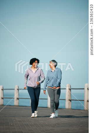 Exercise, walking and senior women by ocean for healthy body, wellness and cardio on promenade. Sports, friends and happy female people in conversation on boardwalk for fitness, training and workout 136361410