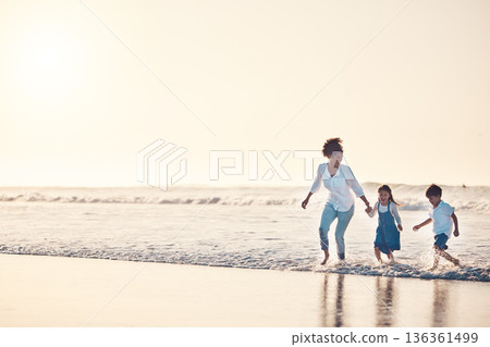 Playing, mother and children at beach on a fun family vacation, holiday or nature adventure at sunset. Young boy and girl holding hands with a woman outdoor for fun energy, happiness and banner space 136361499