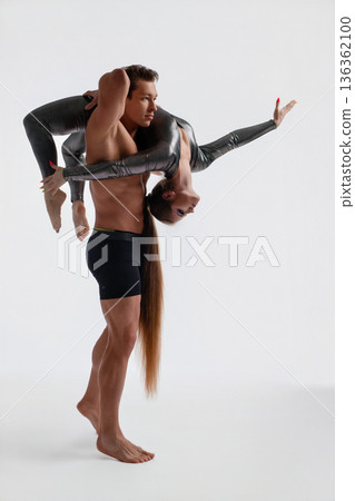 Strong man lifting a flexible woman in an acrobatic pose against a white studio background. Strong man lifting a flexible woman in an acrobatic pose against a white studio background. 136362100