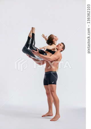 Strong man lifting graceful woman in a dynamic acrobatic pose in a studio. Strong man lifting graceful woman in a dynamic acrobatic pose in a studio. 136362103