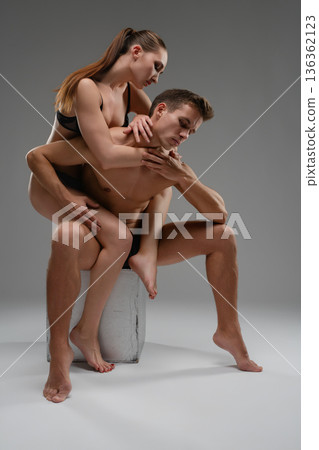 An artistic portrait of an intimate couple in a dramatic pose. The woman in black lingerie embraces a man from behind in a studio. An artistic portrait of an intimate couple in a dramatic pose. The woman in black lingerie embraces a man from behind in a studio. 136362123