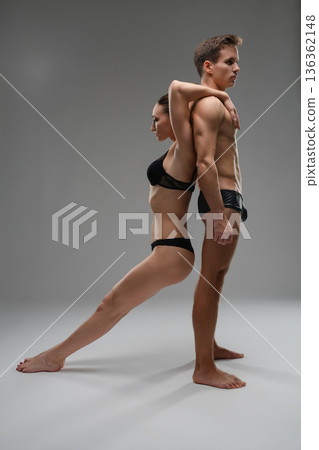 Athletic couple in black underwear in a dramatic acrobatic pose on a gray background. Athletic couple in black underwear in a dramatic acrobatic pose on a gray background. 136362148