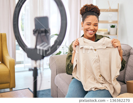 Fashion, live streaming and a black woman influencer unboxing a clothes outfit in her home. Social media, brand deal and a happy female content creator recording a broadcast for subscription service Fashion, live streaming and a black woman influencer unboxing a clothes outfit in her home. Social media, brand deal and a happy female content creator recording a broadcast for subscription service 136362270