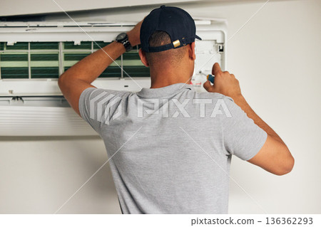 Maintenance, air conditioner and man with screwdriver for problem solving on machine from back. Aircon, ac repair and handyman service with technician, electrician or contractor work on ventilation. 136362293