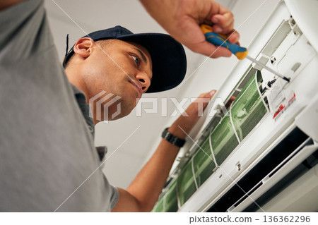 Maintenance, air conditioner and man with screwdriver for problem solving on machine from below. Aircon, ac repair and handyman service with technician, electrician or contractor work on ventilation 136362296