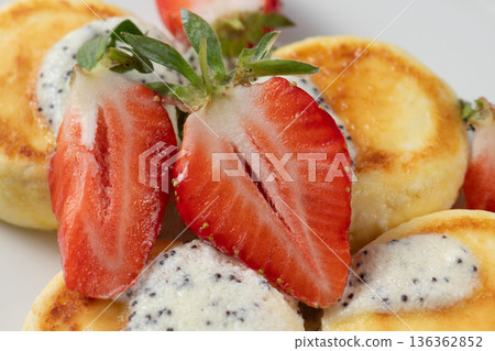 Delicious curd pancakes with poppy seeds and fresh strawberries decorating a plate Delicious curd pancakes with poppy seeds and fresh strawberries decorating a plate 136362852