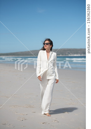 Businesswoman walking on the beach wearing white suit and sunglasses Businesswoman walking on the beach wearing white suit and sunglasses 136362860