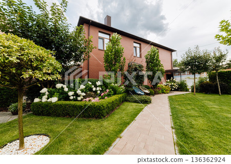 Landscaped garden with brick house, paver walkway, lawn, hydrangeas and outdoor chairs 136362924