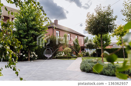 Sunlit brick house courtyard with hanging chair and manicured garden landscape Sunlit brick house courtyard with hanging chair and manicured garden landscape 136362937
