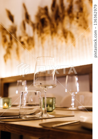 Elegant restaurant table with wine glasses, candles and pampas grass backdrop 136362979