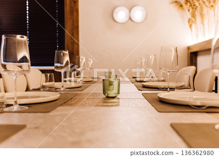 Elegant long dining table set with wine glasses and warm ambient light Elegant long dining table set with wine glasses and warm ambient light 136362980