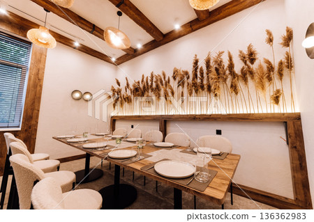 Cozy boho private dining room with pampas wall, set table and rattan lights 136362983