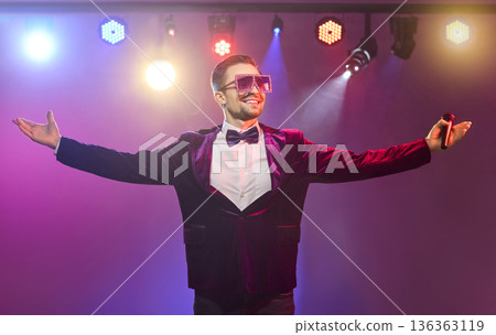 Confident presenter with arms wide on stage under bright vivid concert lights Confident presenter with arms wide on stage under bright vivid concert lights 136363119