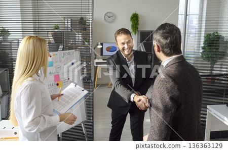 Smiling executives handshake after financial briefing in bright modern office Smiling executives handshake after financial briefing in bright modern office 136363129