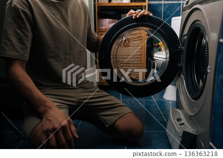 Person inspecting and removing lint filter from front-loading washing machine or tumble dryer, ensuring proper cleaning and essential appliance maintenance for optimal performance. 136363218