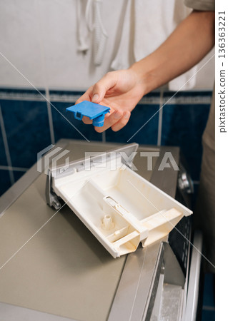 Human hand holding washing machine detergent tray component, preparing to clean drawer to remove accumulated soap residue and prevent blockages, ensuring proper functioning for laundry chores. Human hand holding washing machine detergent tray component, preparing to clean drawer to remove accumulated soap residue and prevent blockages, ensuring proper functioning for laundry chores. 136363221