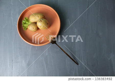 Potato tubers on a plate and fork on a gray background Upper angle view from above with space for copyspace text. Raw food concept 136363492