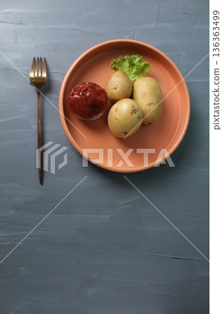 Served lunch, raw potatoes on a plate, fork, napkin on a gray background with space for copyspace text. The concept of vegetarianism, rejection of meat and fish Served lunch, raw potatoes on a plate, fork, napkin on a gray background with space for copyspace text. The concept of vegetarianism, rejection of meat and fish 136363499