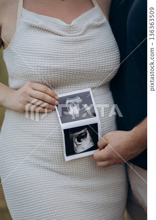 Pregnant couple holding ultrasound photos on baby bump, expecting parents 136363509