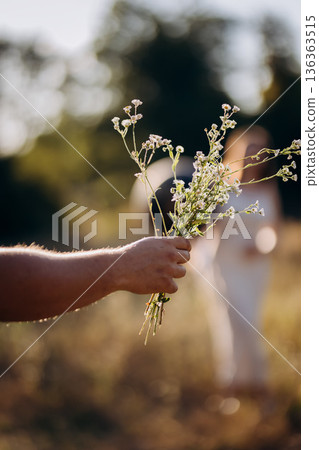Hand offering wildflower bouquet to woman at sunset, romantic moment Hand offering wildflower bouquet to woman at sunset, romantic moment 136363515