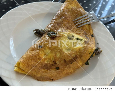 Omelette served on a white plate with a fork, featuring herbs and mushrooms 136363596