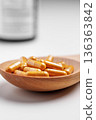 Golden herbal capsules placed in a wooden spoon. Dietary supplement on white table with pills bottle on background 136363842