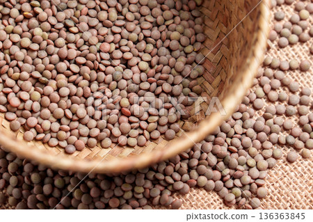 Dry brown lentils in wicker container on natural jute cloth. Plant based protein source. Uncooked diet ingredient 136363845