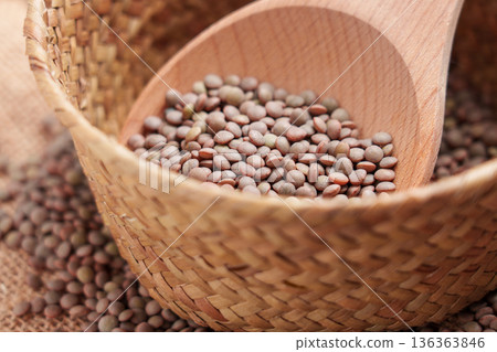 Brown lentils inside woven bowl with wooden scoop. Traditional pantry staple for wholesome meals. 136363846